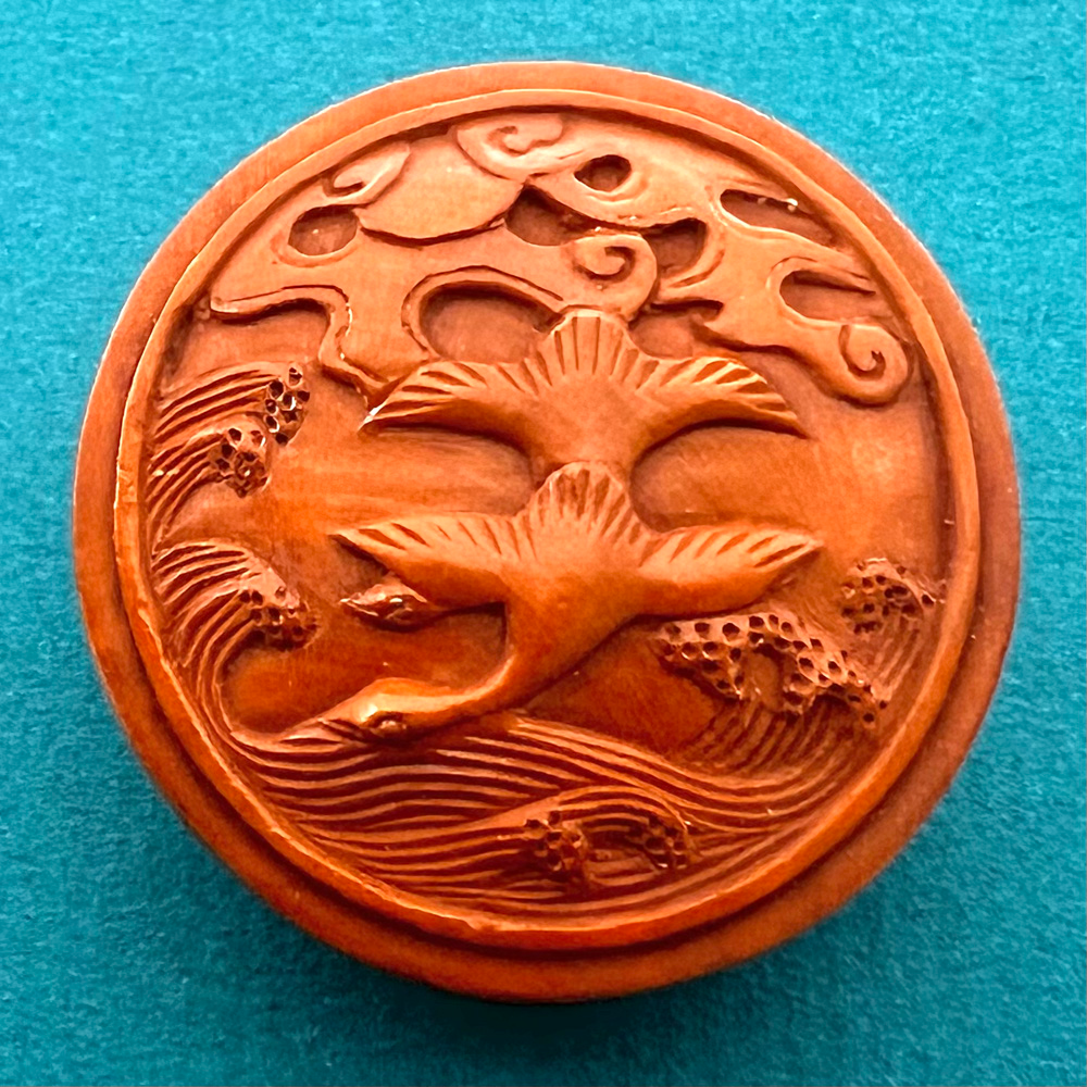 Boxwood button of two geese flying over water.
