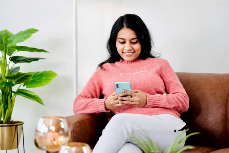 Woman-sitting-on-couch-and-smiling-at-phone