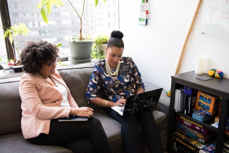 Two women sitting on couch working on laptop