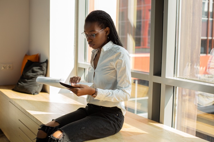 Woman sitting down next to window reading a document